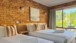 A hotel room with two beds, a brick wall, a painting, a nightstand, and a window with curtains.
