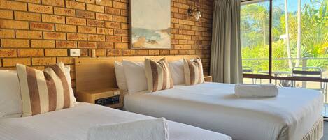 A hotel room with two beds, a brick wall, a painting, a nightstand, and a window with curtains.