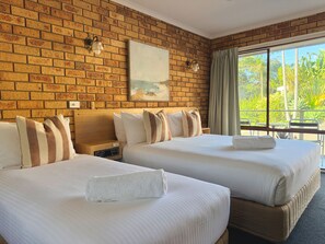 A hotel room with two beds, a brick wall, a painting, a nightstand, and a window with curtains. - Ocean View Motor Inn (Merimbula)