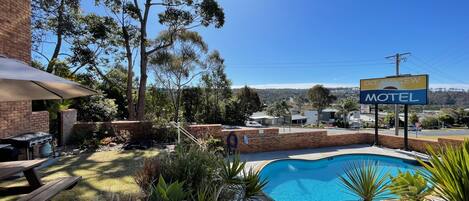 Un motel con piscina rodeada de plantas, zona de barbacoa y vistas del paisaje.