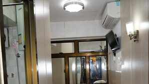 Une petite pièce comprenant un lit, une chaise, une petite table, un miroir et un appareil de climatisation.