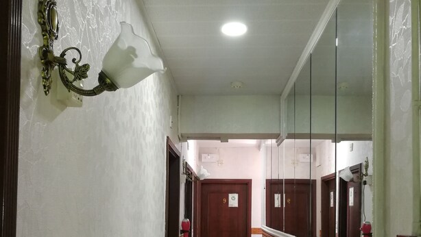Un couloir avec une porte en bois portant le numéro « 9 », un extincteur et un miroir accroché au mur.