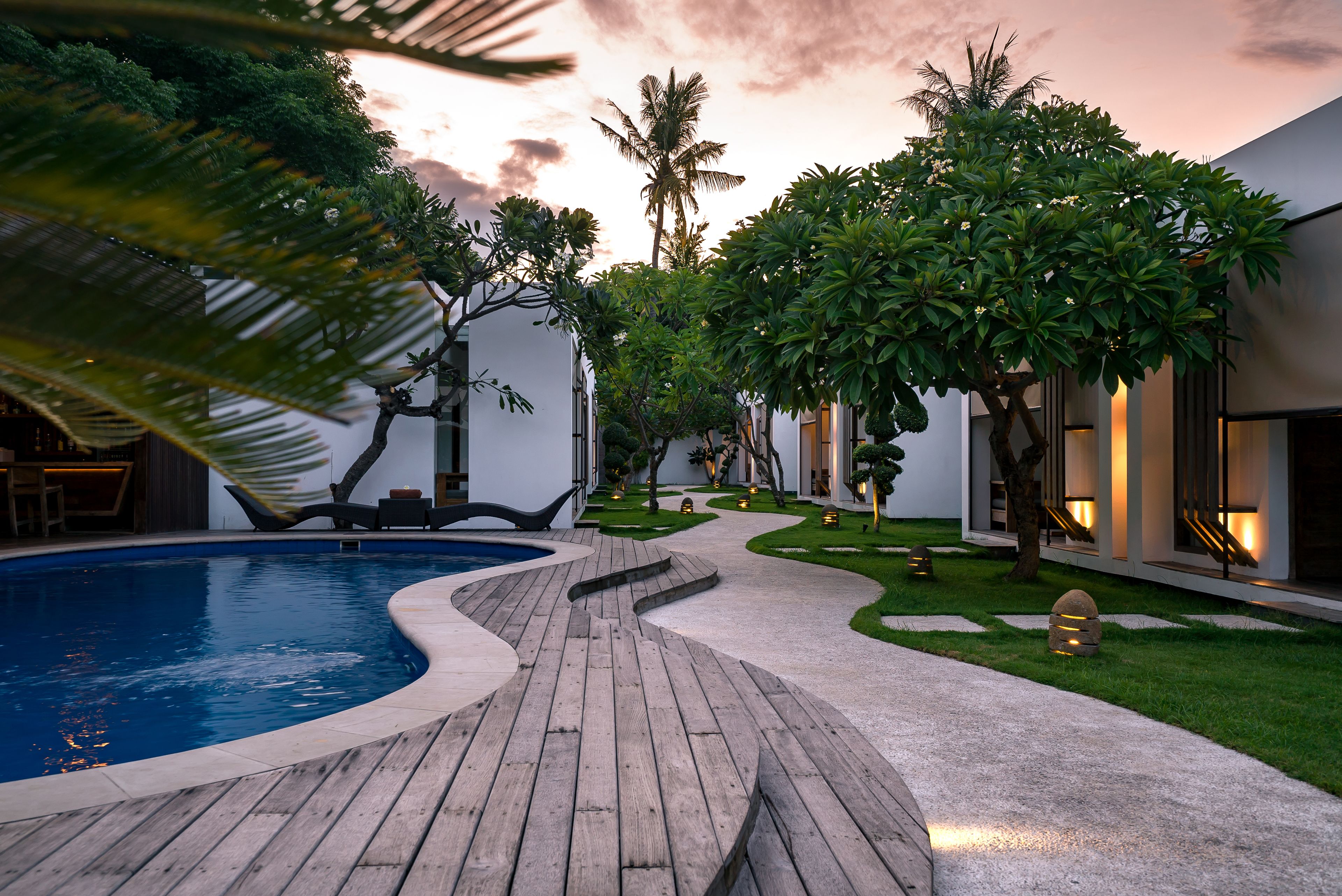 Un área de piscina con cubierta de madera, rodeada de abundante vegetación y palmeras.