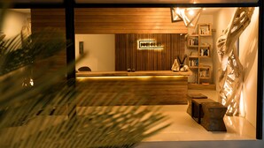 A reception area with a wooden reception desk, a bookshelf, and a decorative wall piece. - Villa Nero (Gili Trawangan)