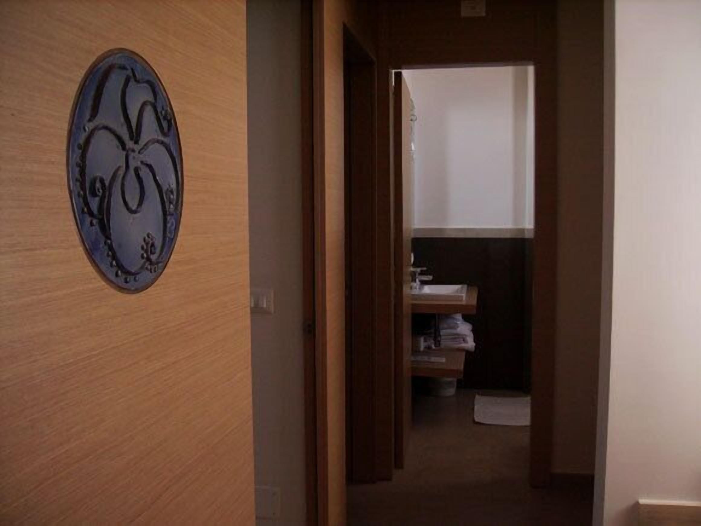 Een hal met een houten deur en een ronde wandversiering. Er is een klein plankje met opgevouwen handdoeken en een witte muur op de achtergrond.