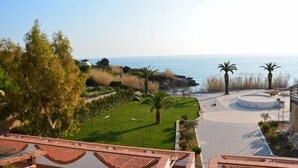 Zona enjardinada amb vista al mar, palmeres i una zona pavimentada circular.