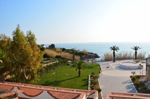Un área ajardinada con vista al mar, palmeras y un espacio pavimentado circular.