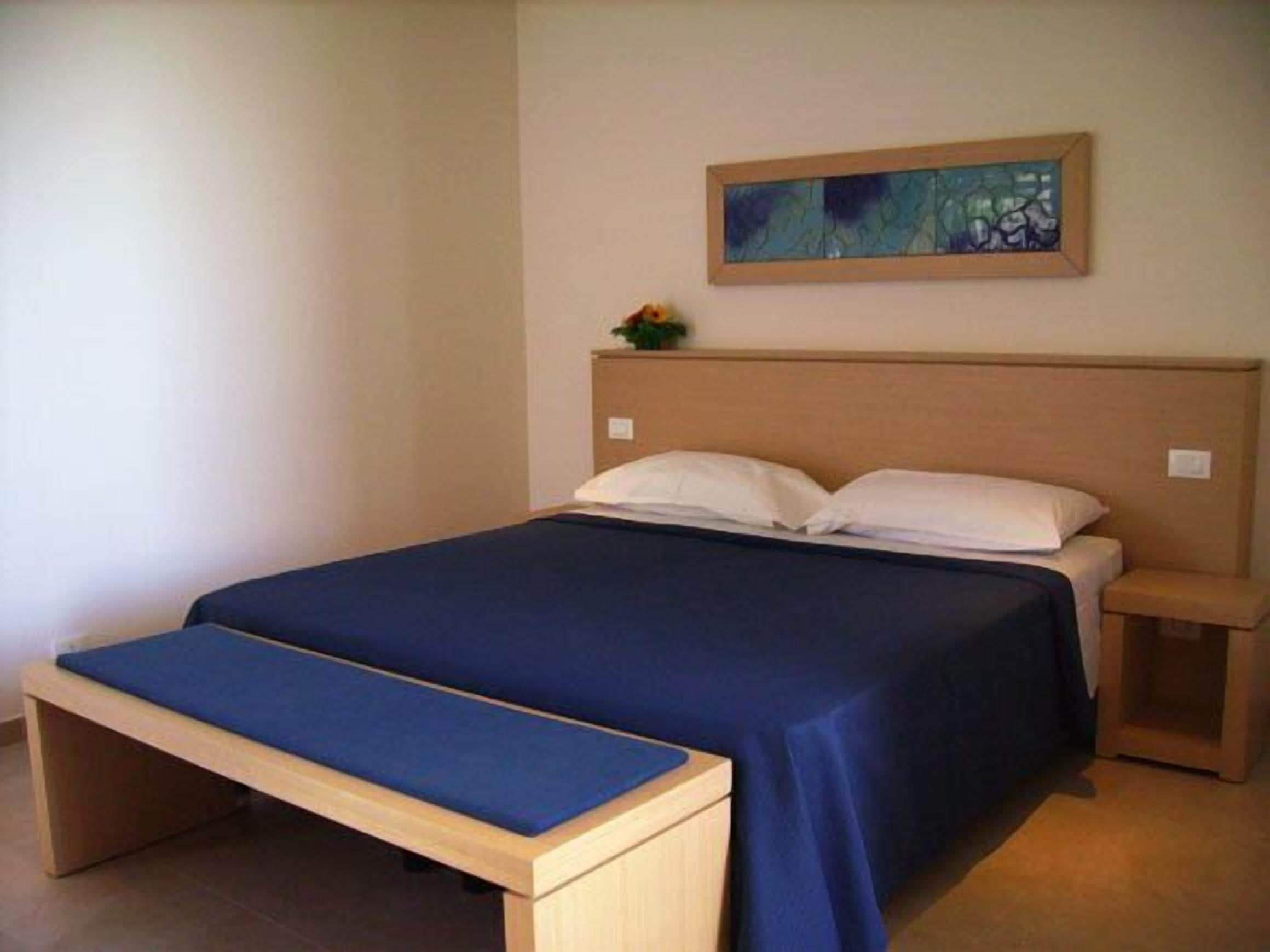 Ein Einzelbett mit Holz Kopfteil, ein Nachttisch und eine Bank.
