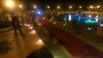 Un área de piscina nocturna con un camino de alfombra roja y velas iluminadas.