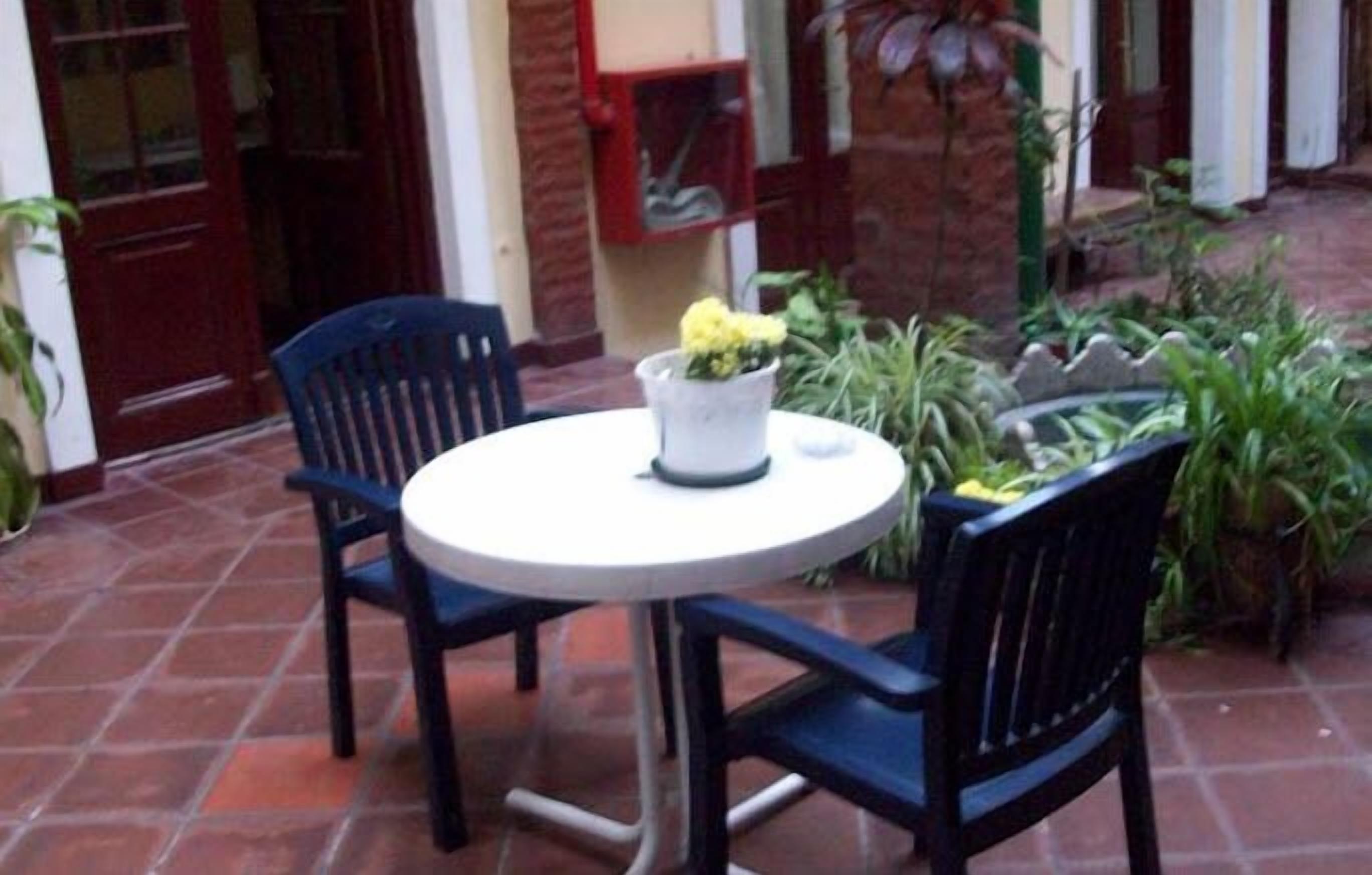 En patio med et rundt bord og to stole, omgivet af krukker med planter og en murstensmur.