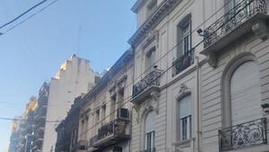 A row of multi-story buildings with balconies, storefronts, and a clear sky. - Santino Recoleta (Buenos Aires)