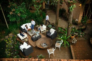 An outdoor patio area with seating arrangements, a fire pit, and lush greenery.