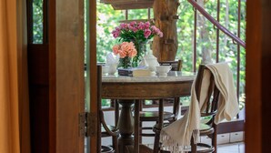 A wooden dining table with a vase of flowers, a book, and a bowl. - Vanā Som (Mae Rim)