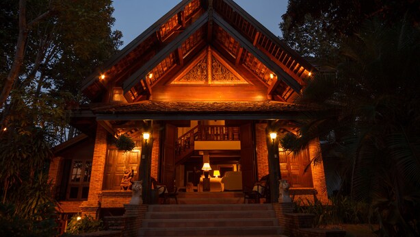 A traditional wooden building with a central staircase, surrounded by lush greenery. - Vanā Som (Mae Rim)