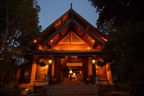 A traditional wooden building with a central staircase, surrounded by lush greenery. - Vanā Som (Mae Rim)