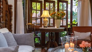 A cozy room with a wooden table, a sofa, and a window with curtains. - Vanā Som (Mae Rim)
