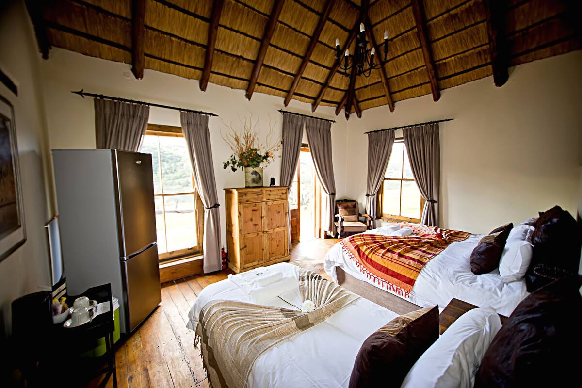 Een slaapkamer met een bed, een dressoir, een stoel, een raam en een koelkast.