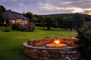 A stone fire pit in a grassy area with a house in the background. - Addo Bush Palace Private Reserve (Addo)