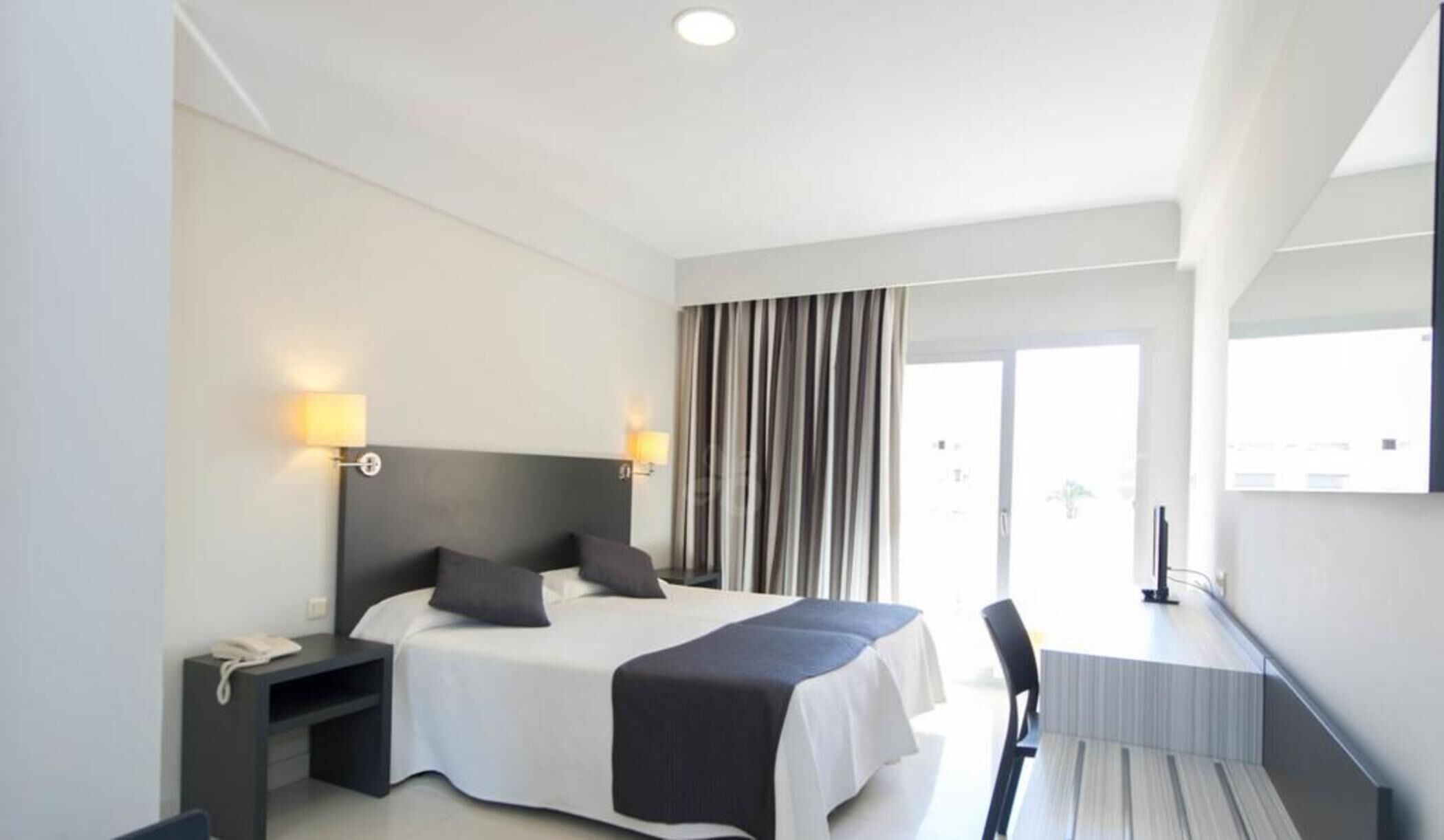 A modern hotel room with a bed, bedside lamps, a desk, and a chair.