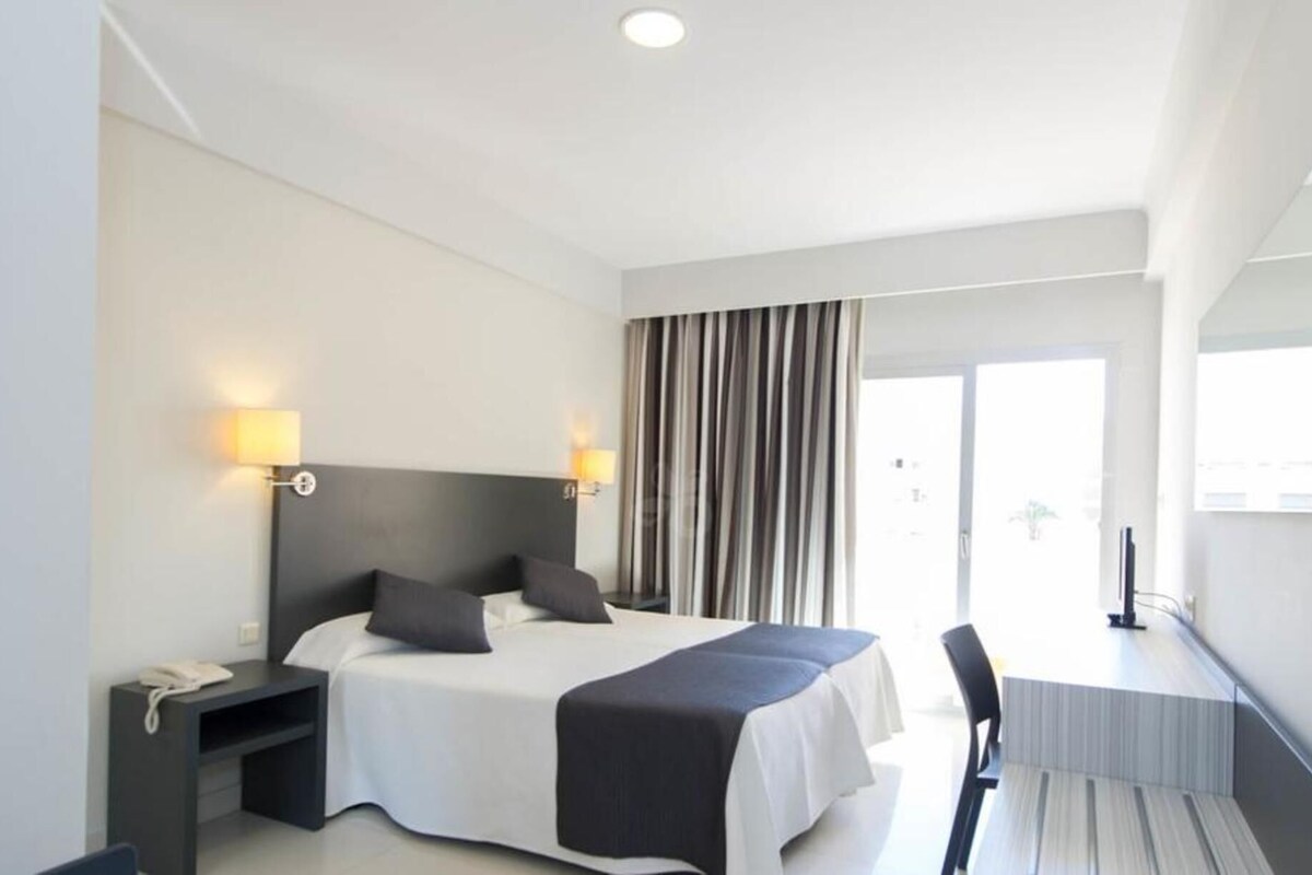 A modern hotel room with a large bed, bedside lamps, a desk, and a chair.