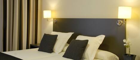 Una camera d'albergo con un letto grande, due abat-jour, un comodino con un'orchidea in vaso e una tenda a righe verticali.