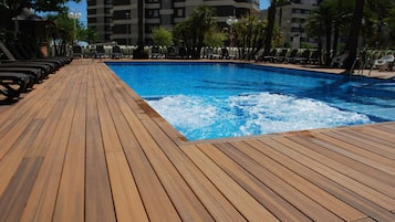 Una terraza de madera que conduce a una piscina con sillas de descanso y palmeras.
