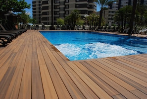 A wooden deck leading to a swimming pool with lounge chairs and palm trees. - Hotel Los Robles (Gandia)