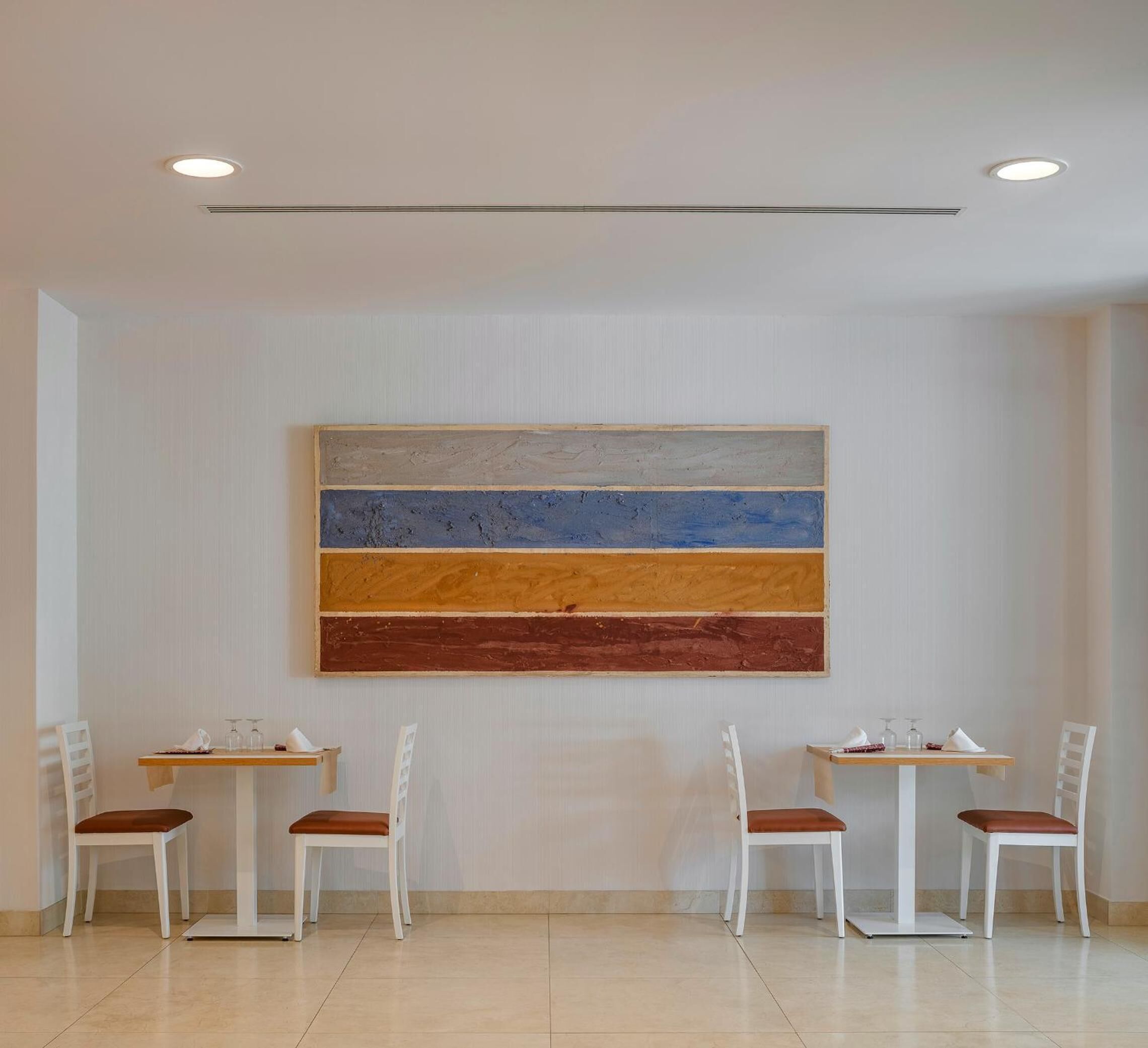 Un comedor con un gran cuadro abstracto en la pared, sillas blancas y una mesa de madera.