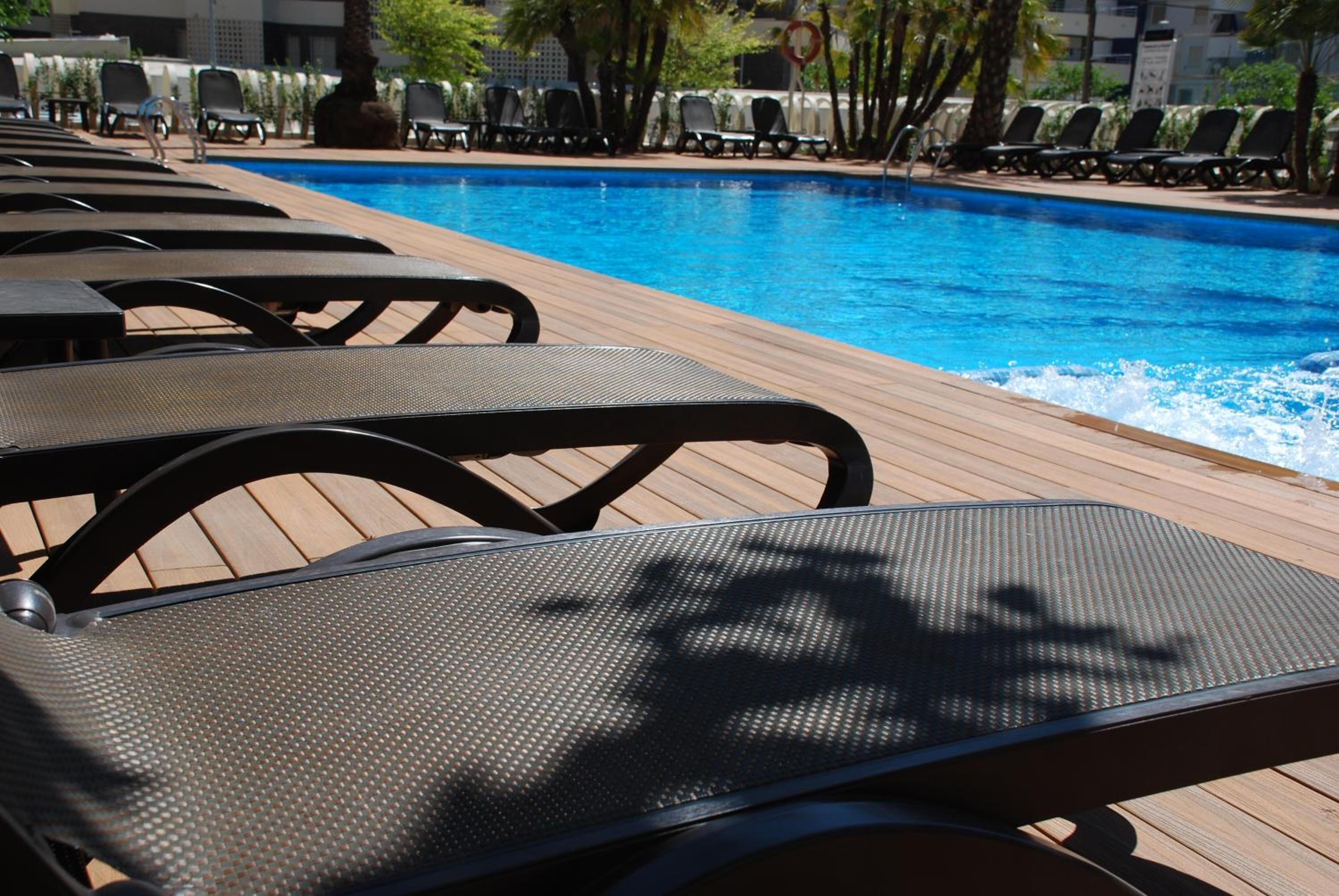 Zona junto a la piscina con sillones de descanso y una terraza de madera.