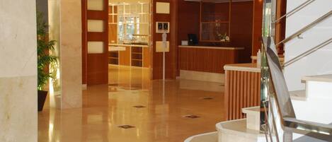 Eine moderne Hotelhalle mit Marmorboden, einer Rezeption und einer Treppe.