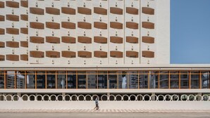 Un edificio moderno con una fachada repetitiva que presenta huecos rectangulares y un largo balcón horizontal con barandillas circulares.