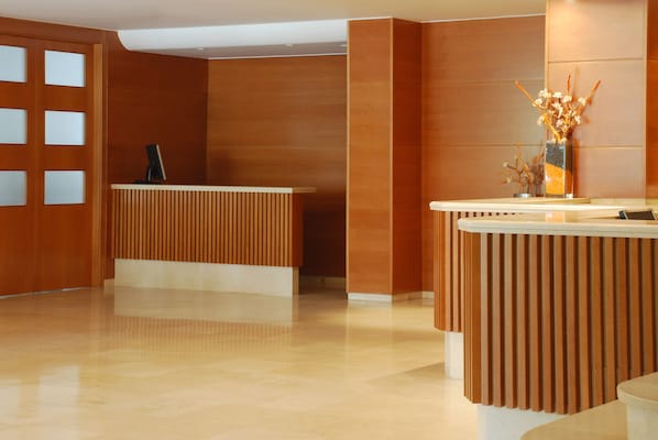Zona de recepción con un mostrador de madera, una barra blanca y un florero con flores secas.