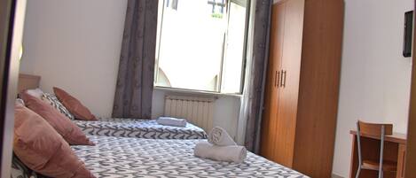 Una camera da letto con due letti, un armadio, una sedia e una finestra con tende.