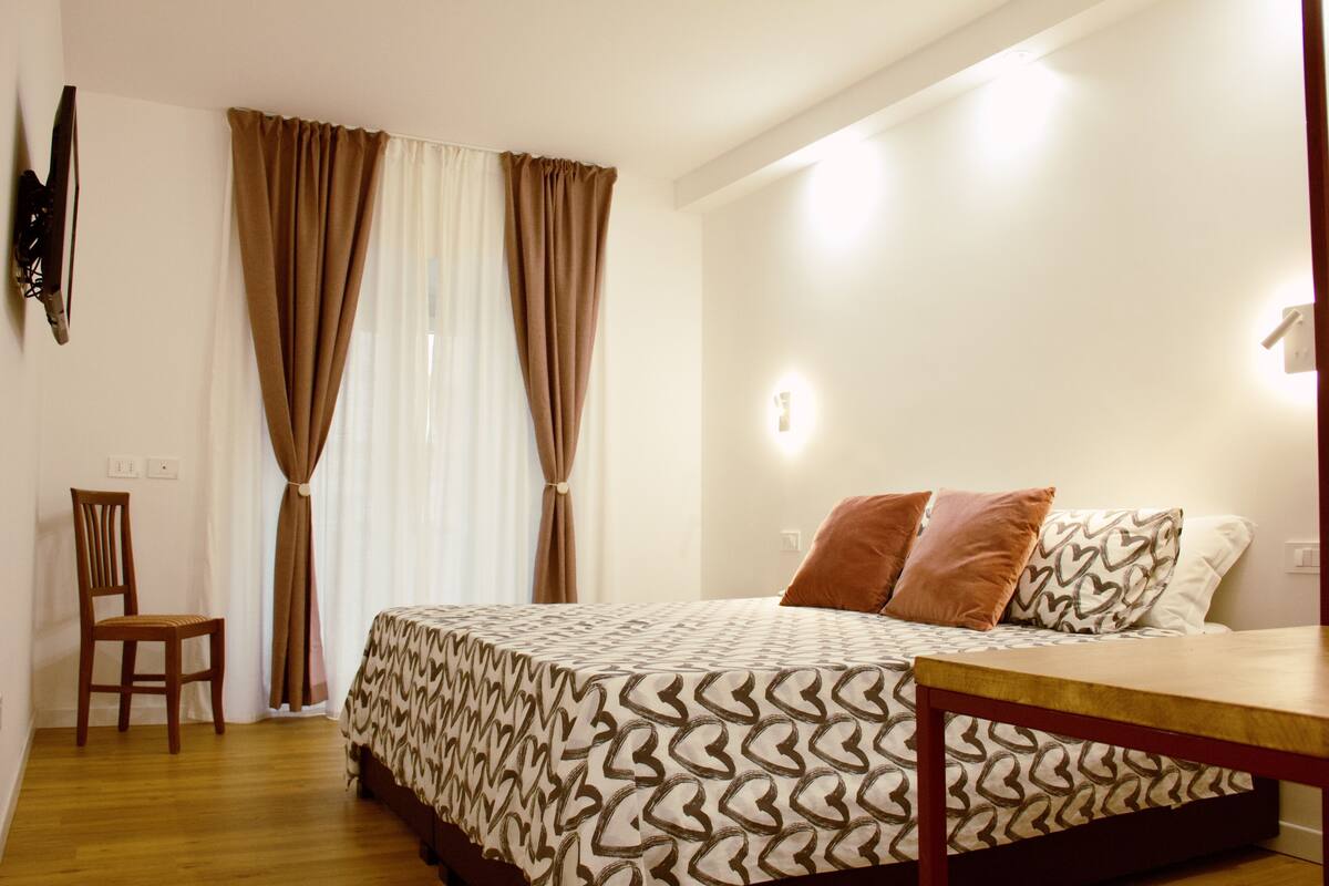 A bedroom with a bed, a wooden chair, a nightstand, and a wall-mounted TV.
