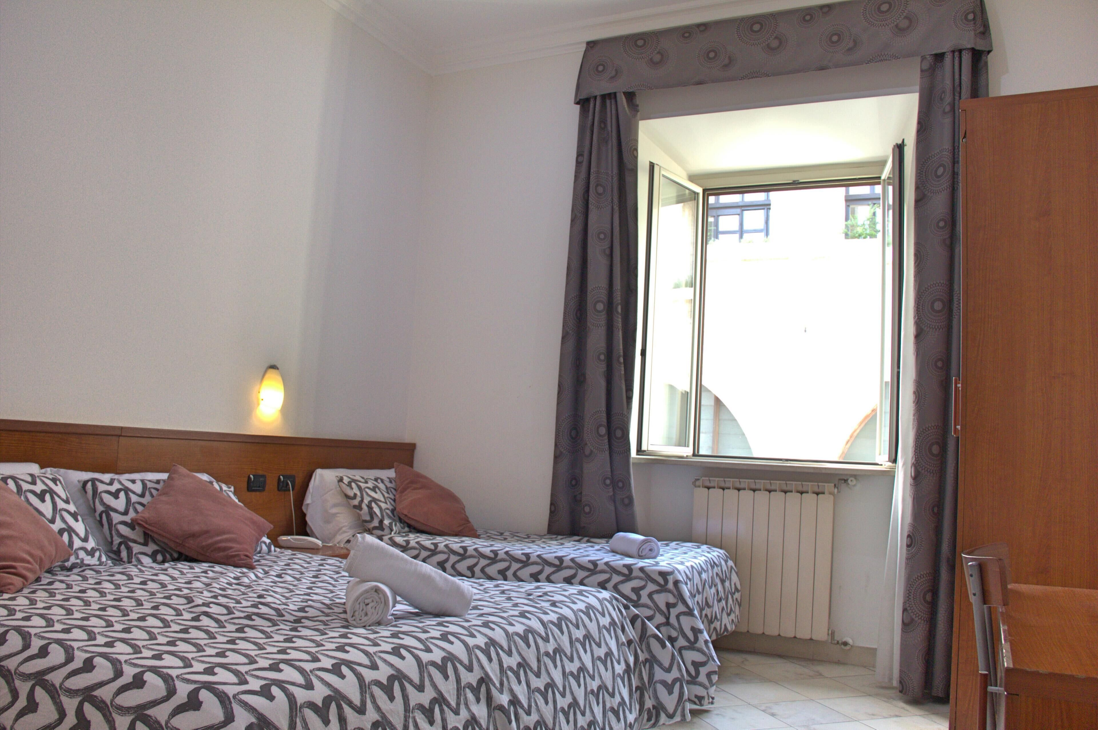 Una habitación de hotel con dos camas, una ventana con cortinas, un radiador y una puerta de madera.