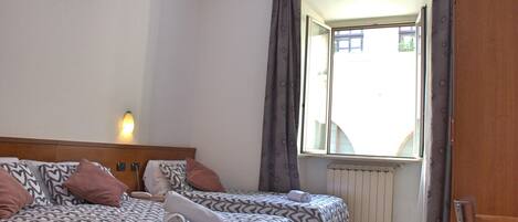 Una habitación de hotel con dos camas, una ventana con cortinas, un radiador y una puerta de madera.