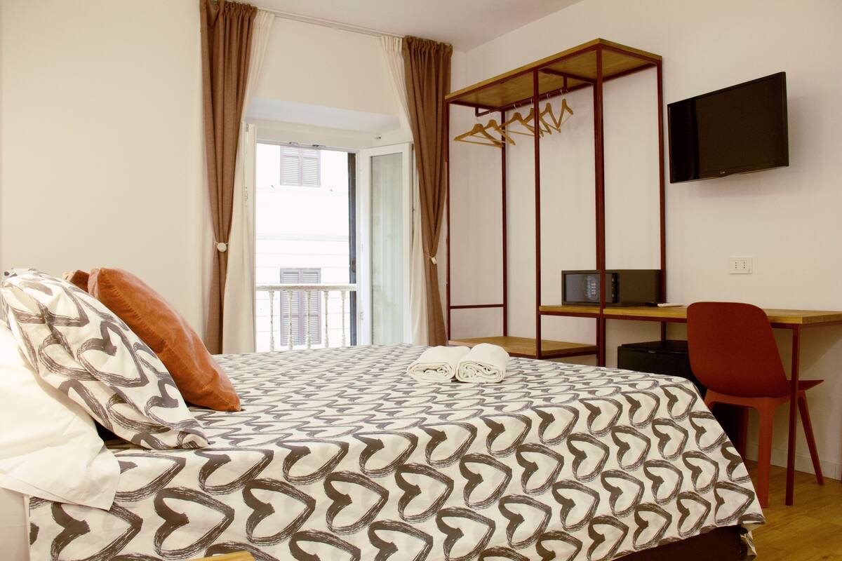 A bedroom with a bed, a desk, a chair, a TV, and a wardrobe.