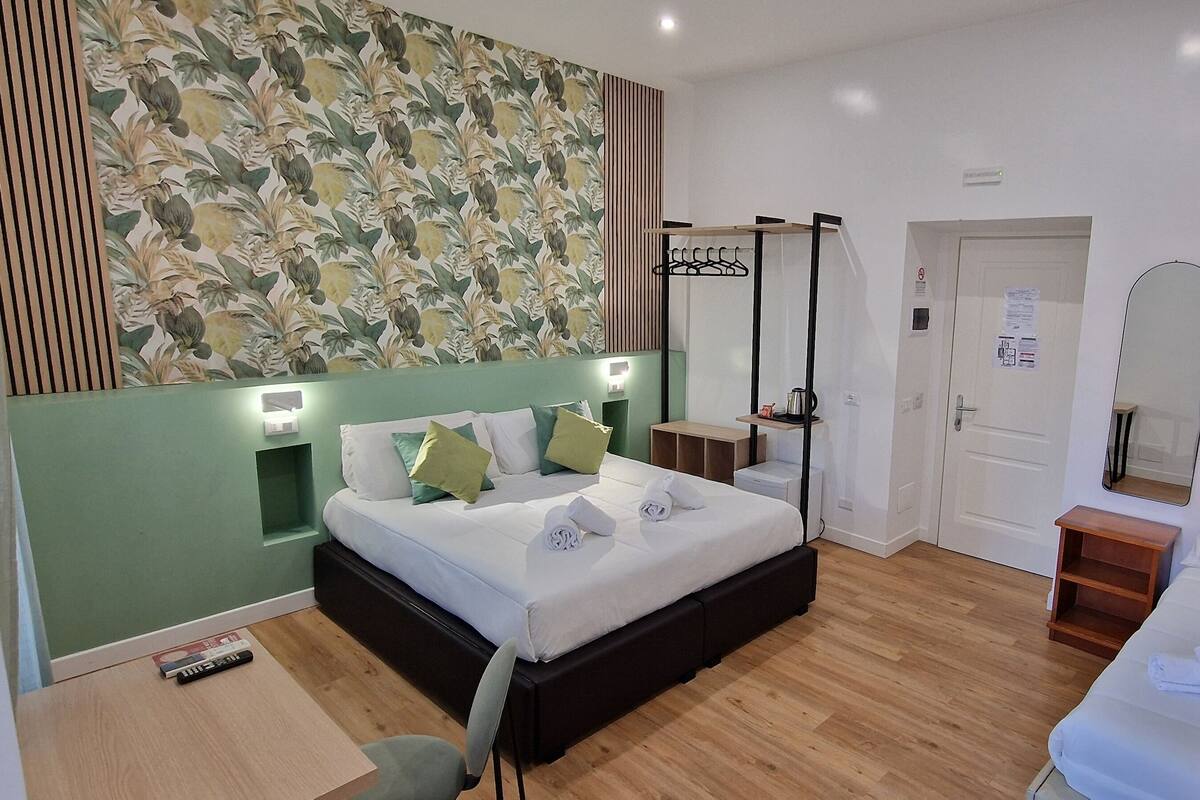 A modern hotel room with a large bed, bedside tables, a mirror, and a wardrobe.