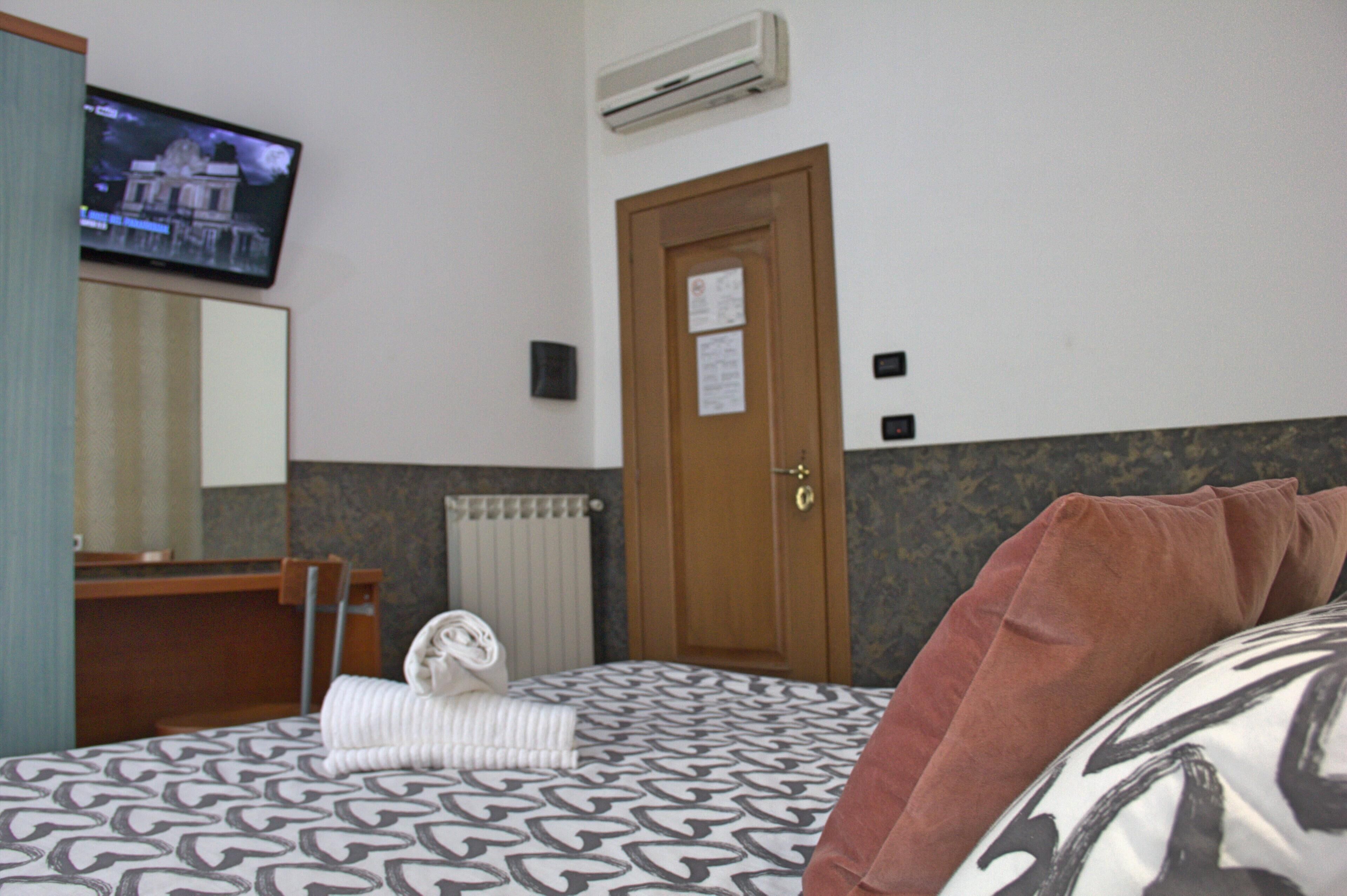 A hotel room with a bed, a desk, a television, and an air conditioning unit.