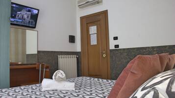 A hotel room with a bed, a desk, a television, and an air conditioning unit.