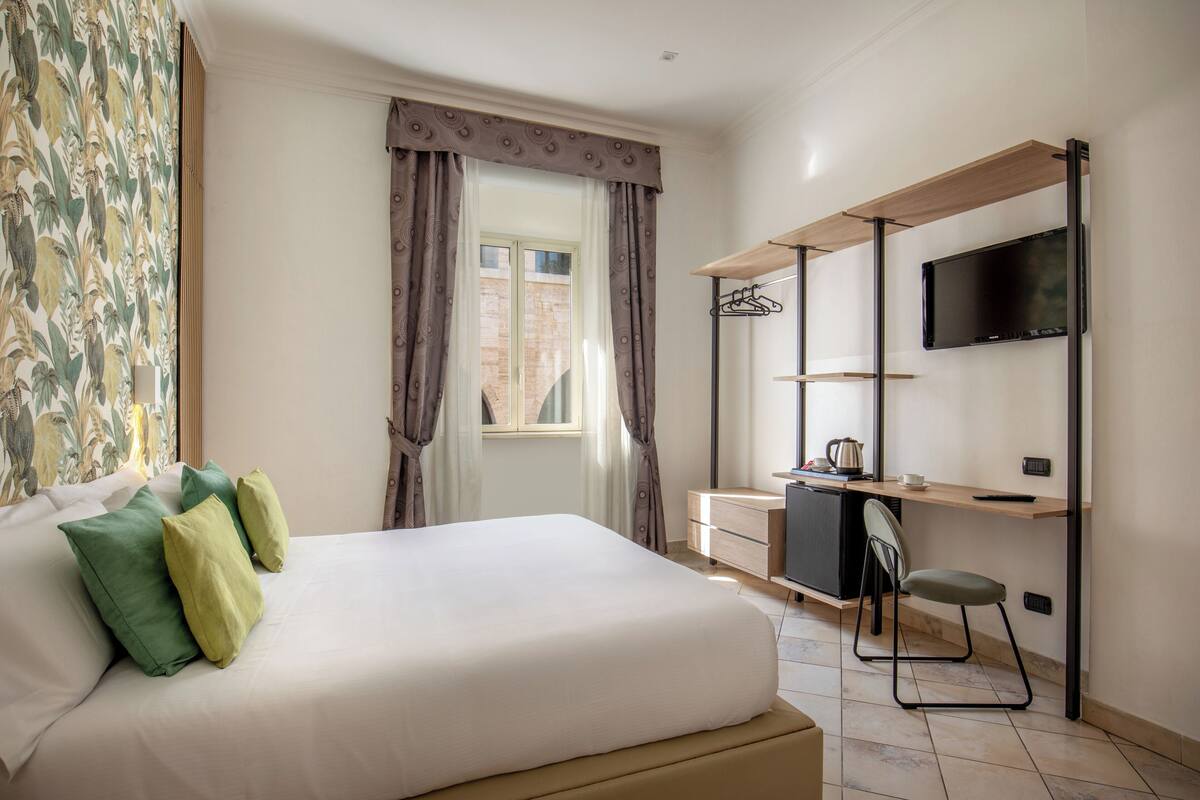 A hotel room with a bed, a desk, a chair, a television, and a window with curtains.