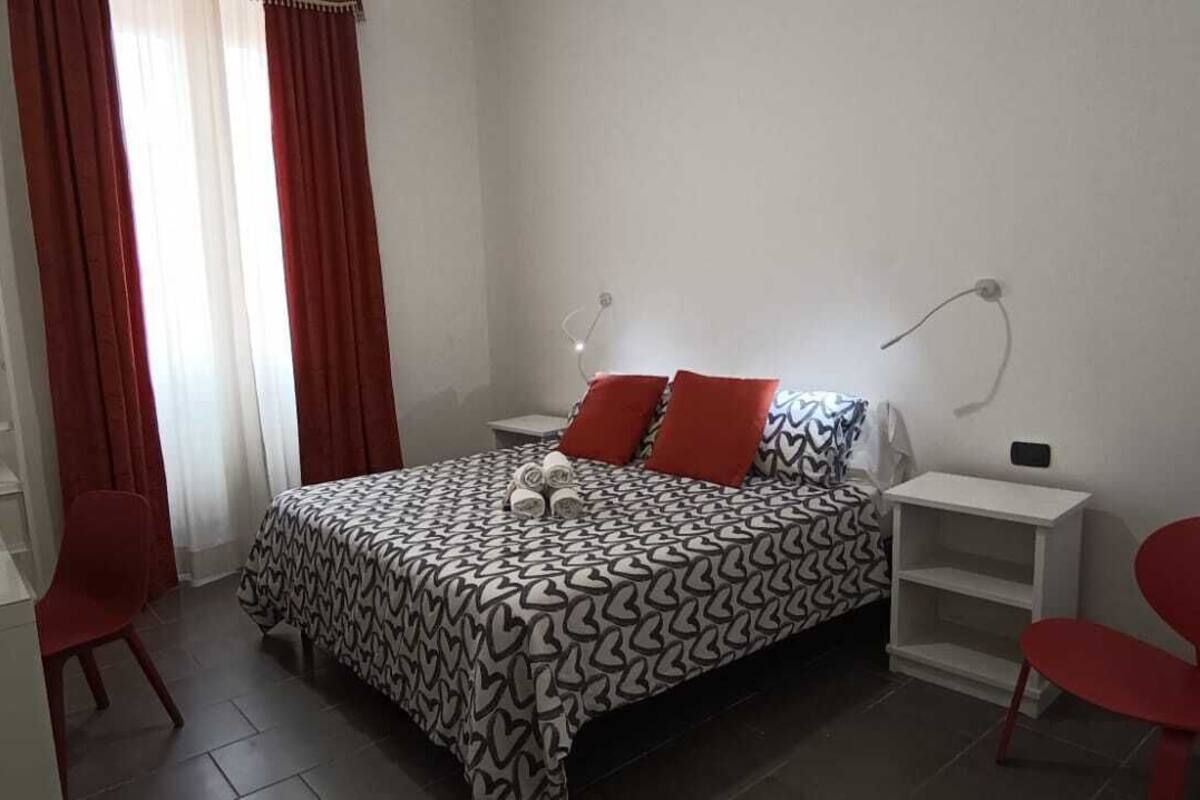 A bedroom with a bed, red chairs, a bedside table, a lamp, and a wardrobe.