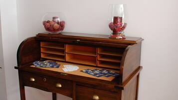 A wooden desk with drawers and a glass vase on top, set against a white wall with two framed pictures.