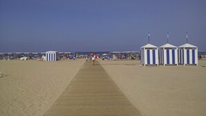 Una playa con un paseo de madera que lleva a cabañas y sombrillas.