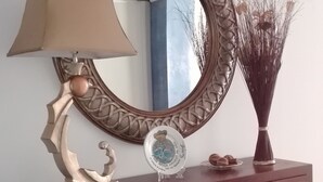 Una consola de madera con un espejo, una lámpara y un florero con ramas.