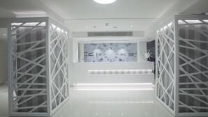 A modern reception area with a central desk, white decorative panels, and a ceiling light. - Princessa Vera Hotel Apartments (Paphos)