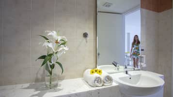 A bathroom with a marble countertop, a white sink, a glass vase with white flowers, and a towel with yellow flowers.