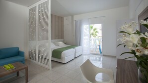 A modern hotel room with a bed, a blue sofa, a wooden coffee table, and a white chair. - Princessa Vera Hotel Apartments (Paphos)