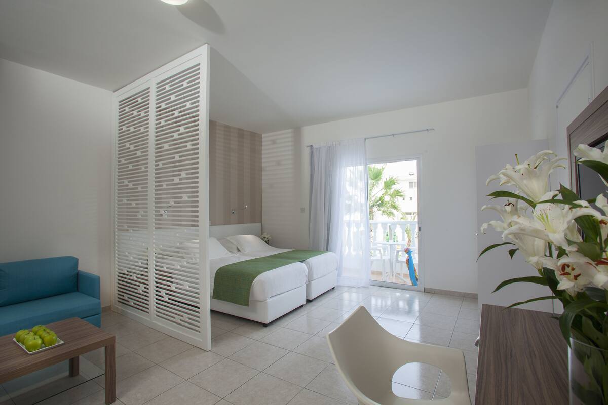 A modern hotel room with a bed, a blue sofa, a wooden coffee table, and a white chair.
