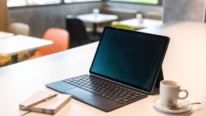 A laptop on a table with a cup of coffee and a notebook.
